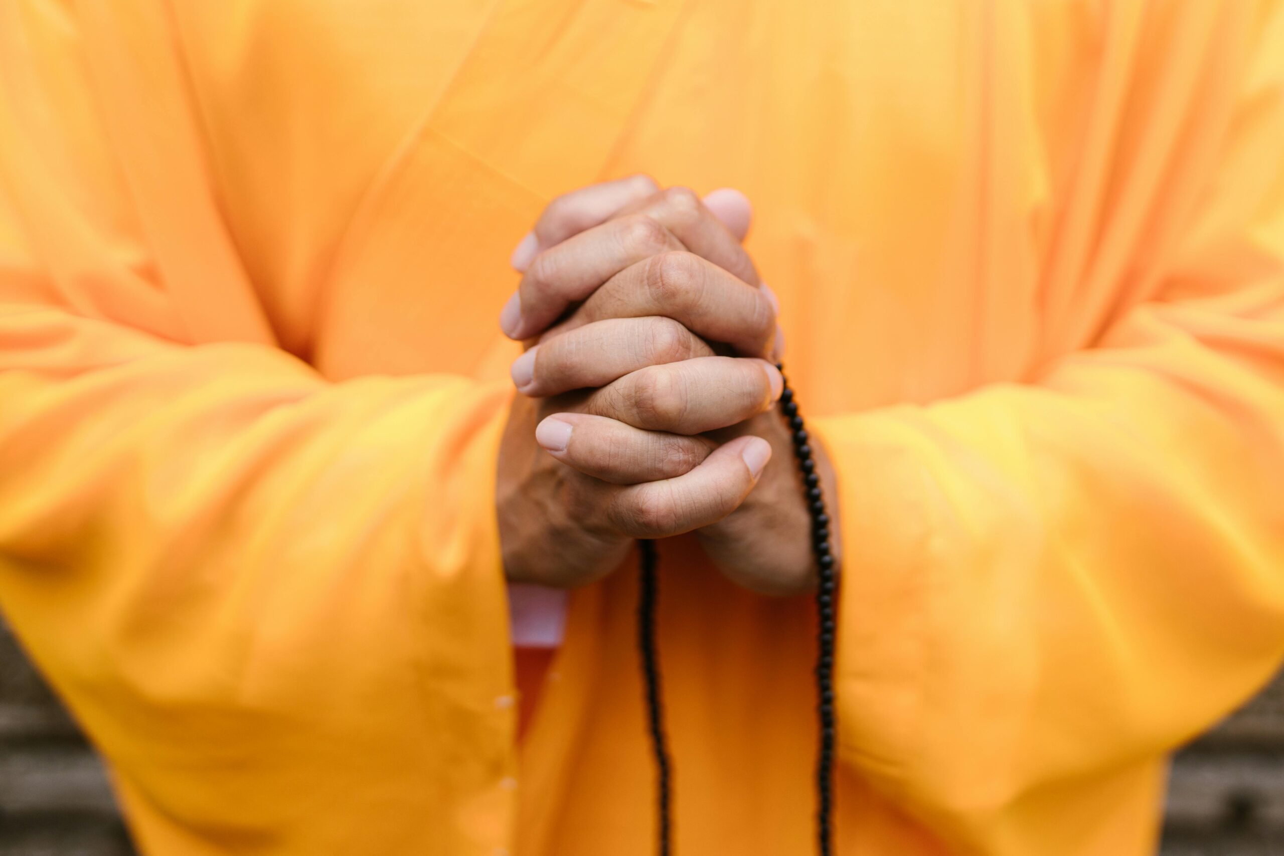 Close-up of hands in prayer wearing yellow robes, sign of Zen meditation and peace.